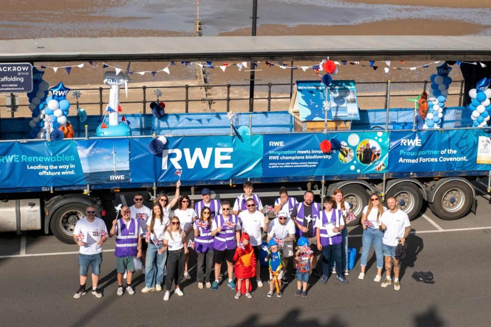 A group of people in British-themed attire posing in front of an RWE promotional truck decorated with balloons and banners.