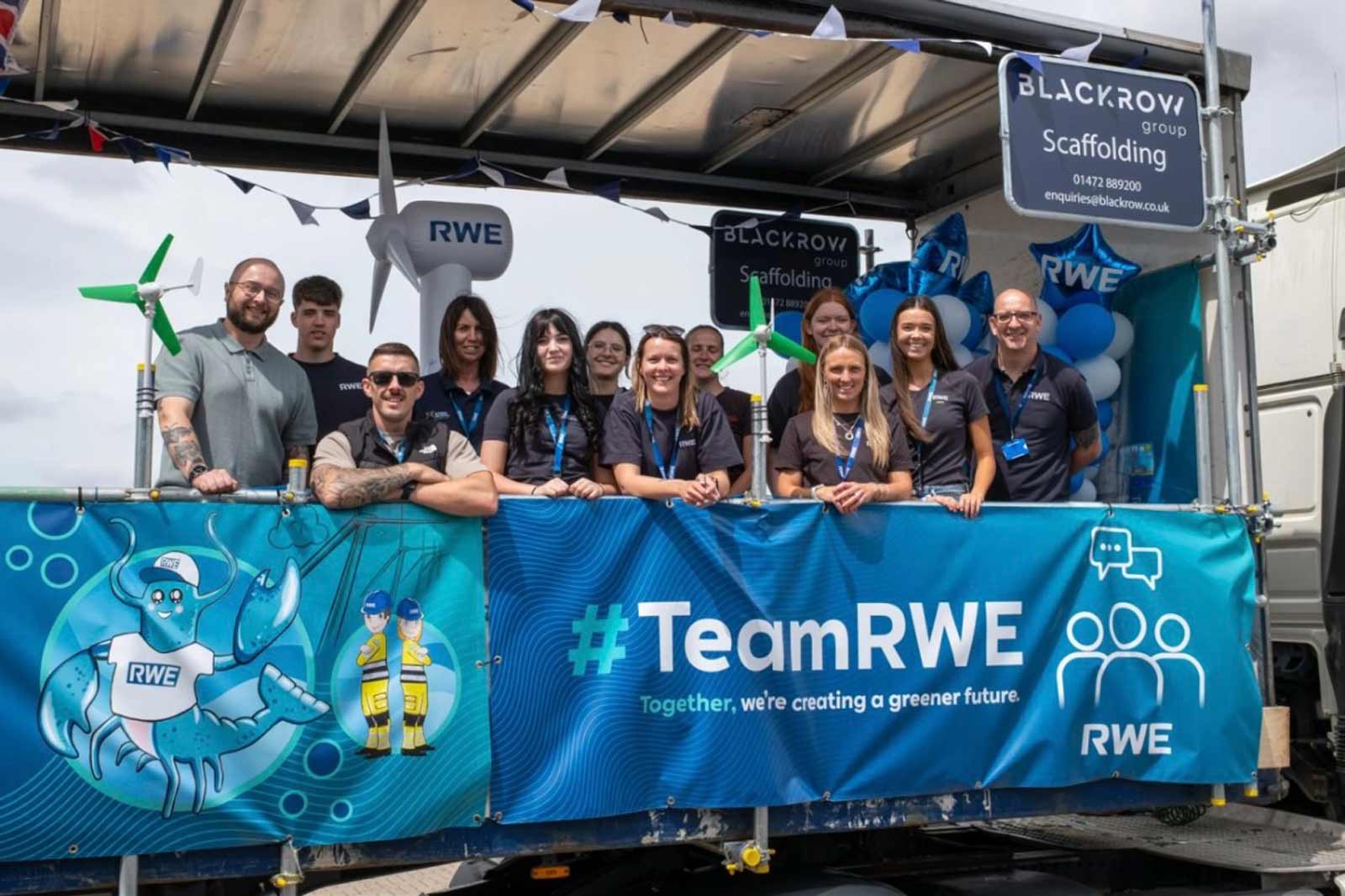 A group of people in branded shirts stand on a trailer, promoting RWE with banners, balloons and wind turbine models.