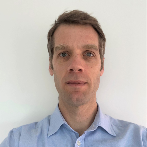 A person wearing a light blue shirt, facing the camera against a plain background.