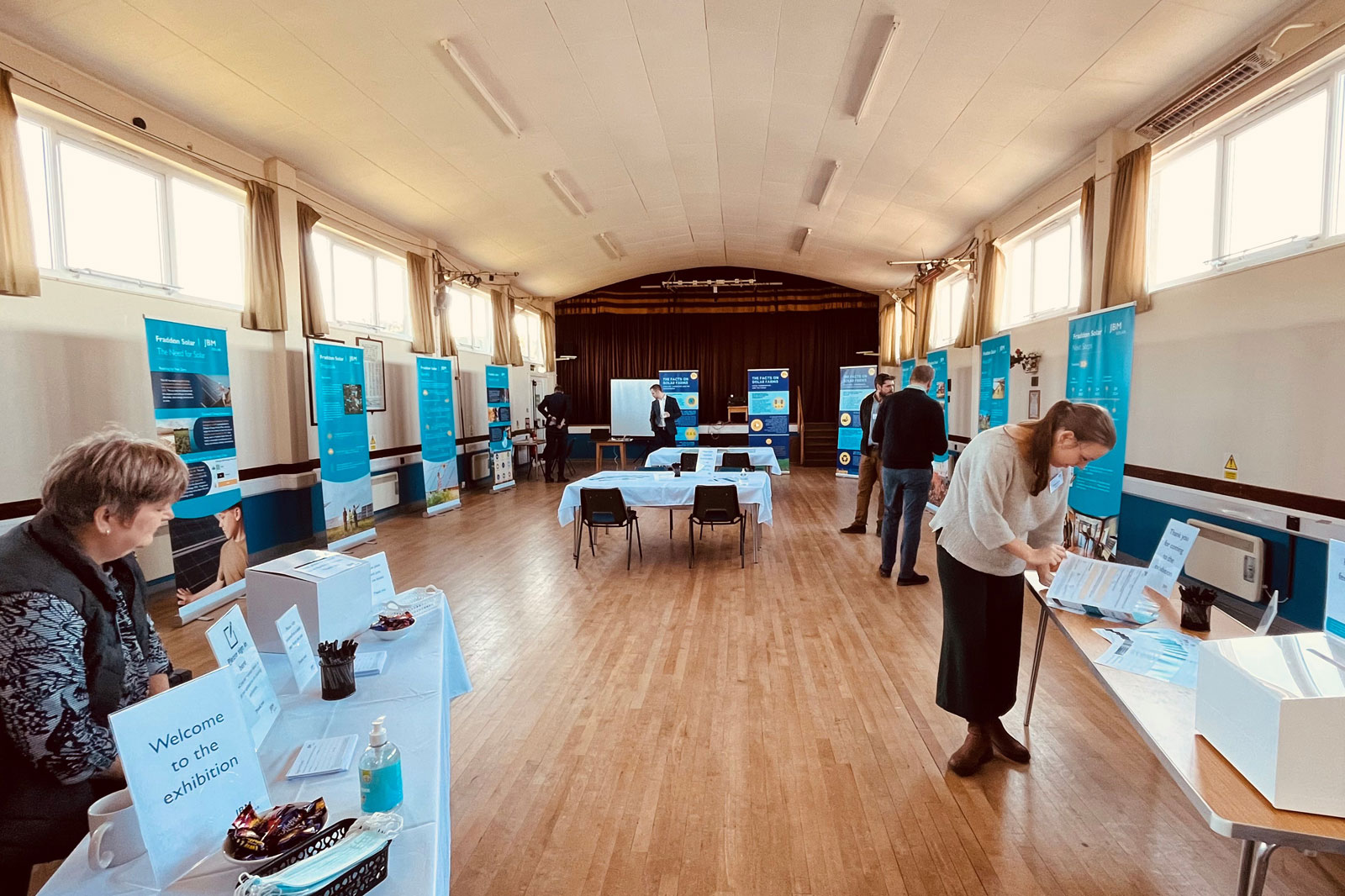 An exhibition space with banners and tables. Visitors engage with displays and informational materials.