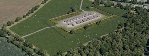 An aerial view of a fenced area with battery storage complex, surrounded by grass and trees, with a field and sheep nearby.