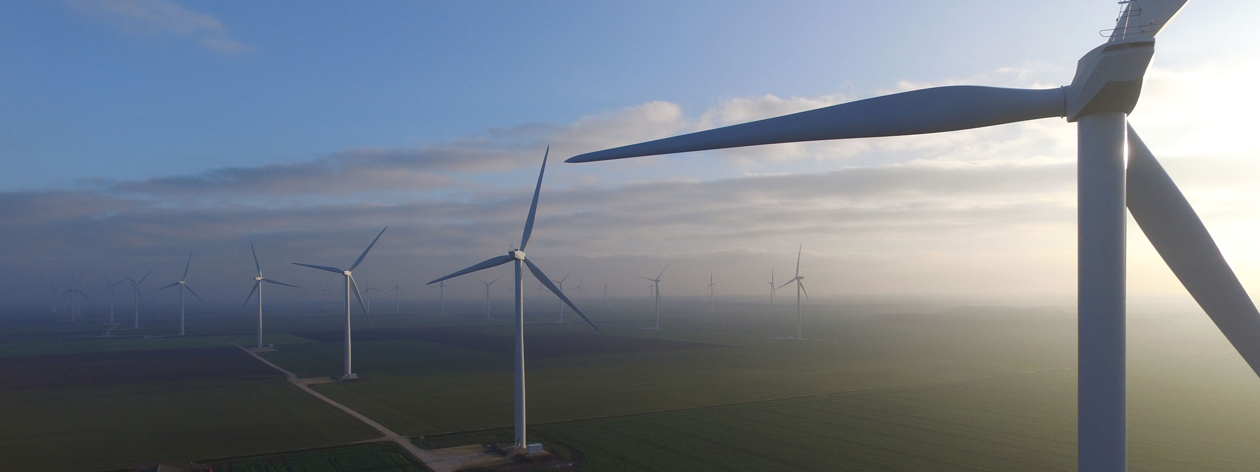 Aerial view of multiple wind turbines in a field under a cloudy sky, showcasing renewable energy production.