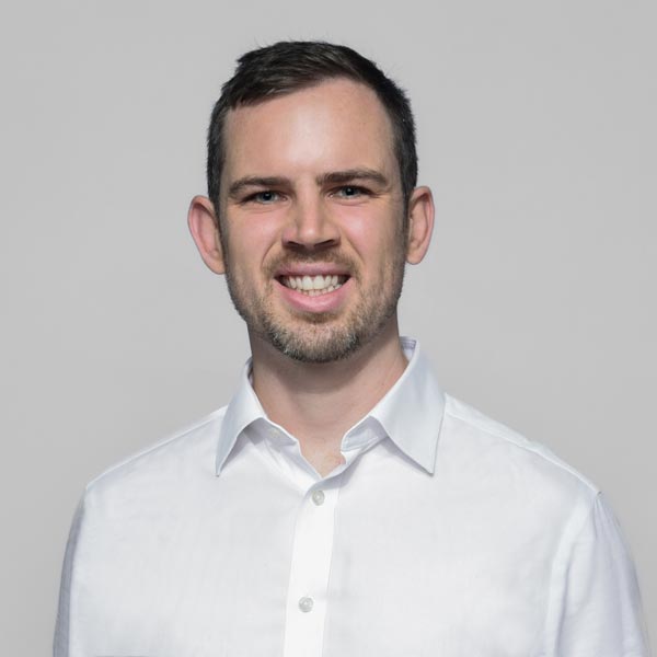 A man wearing a white button-up shirt against a plain grey background, focusing on a neutral expression.