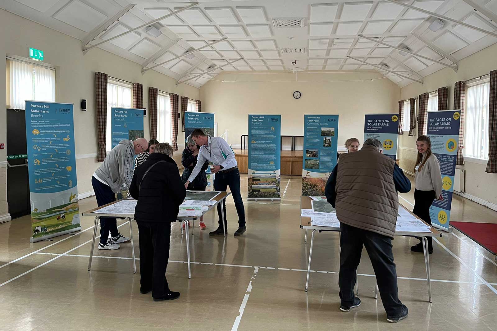 A community meeting about Potters Hill Solar Farm, featuring informative displays and attendees studying plans and brochures.