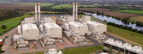 Aerial view of a power plant featuring large structures, cooling towers, and extensive green fields beside a river.