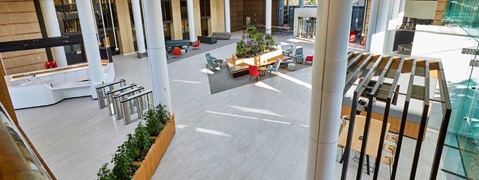 A spacious modern lobby with seating areas, plants, and large windows, featuring white pillars and sleek furniture.