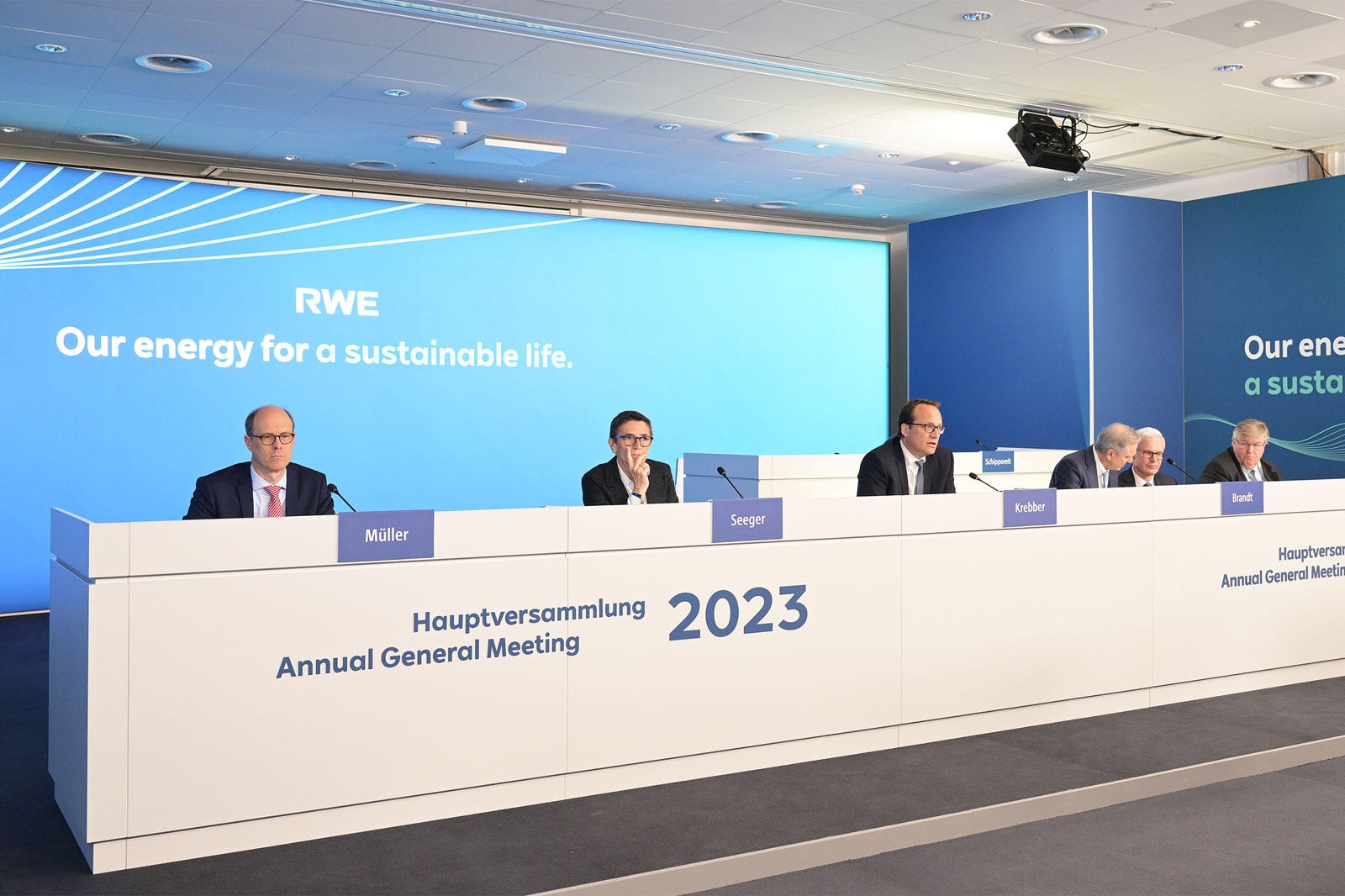The stage featuring the RWE sign and men during the 2023 Annual General Meeting, all looking down at their papers.