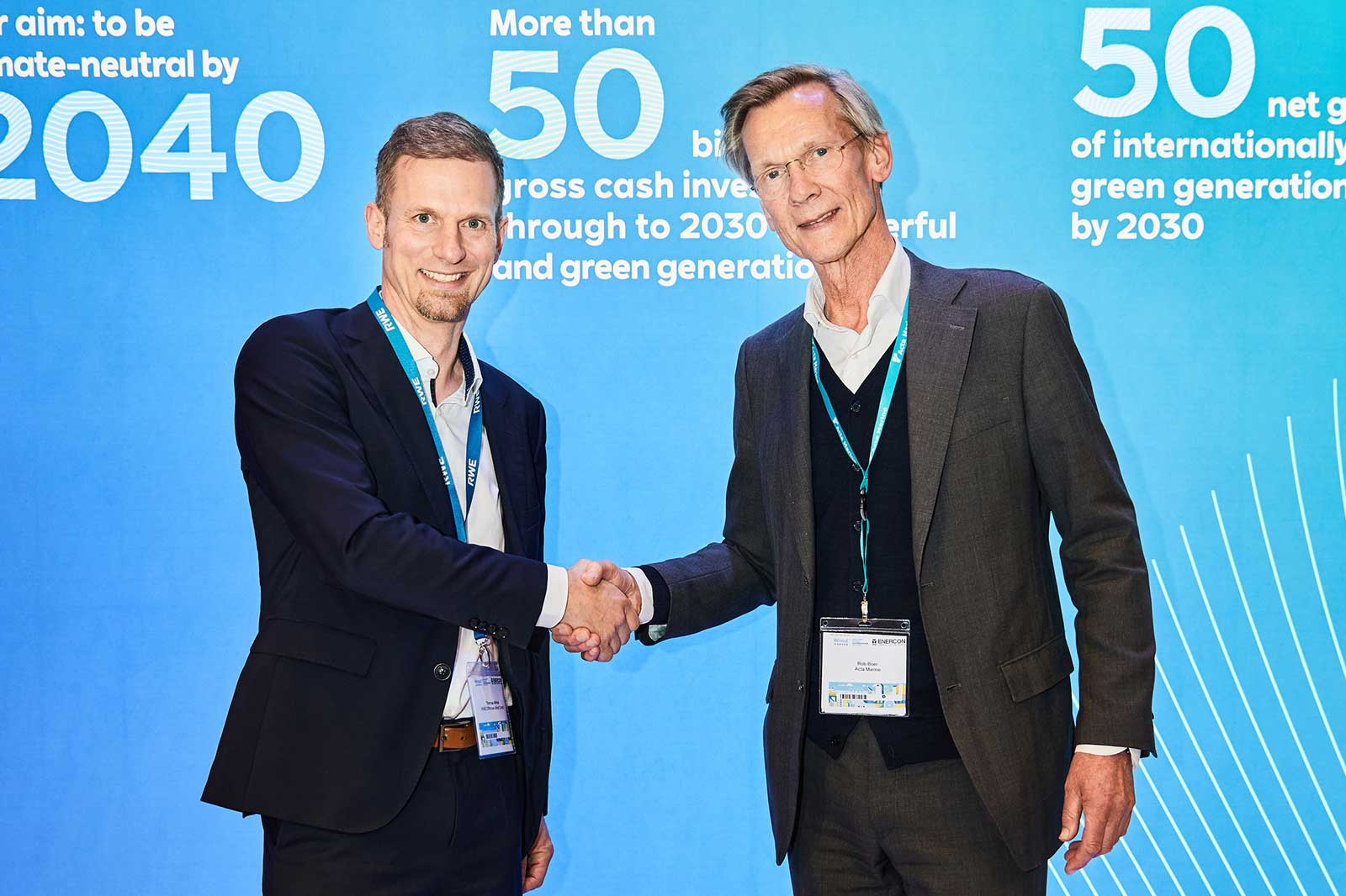 Two men shake hands against a blue backdrop featuring slogans about climate neutrality and green energy investments.
