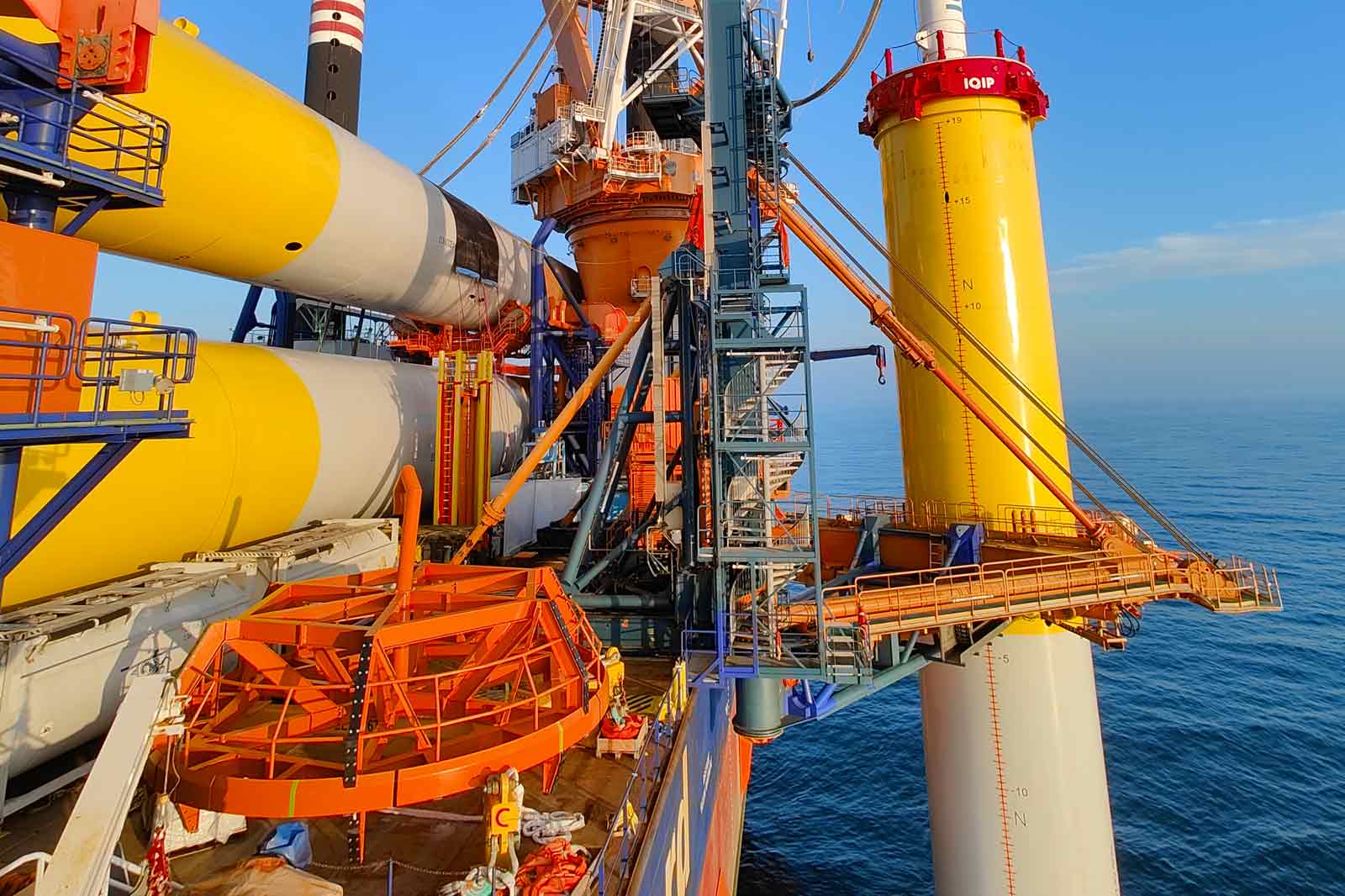 A close-up view of a large offshore oil platform with colourful structures, cranes, and a sea backdrop.
