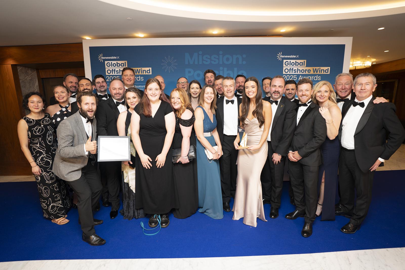 A group of elegantly dressed individuals at the Global Offshore Wind 2025 Awards event, smiling and holding awards.