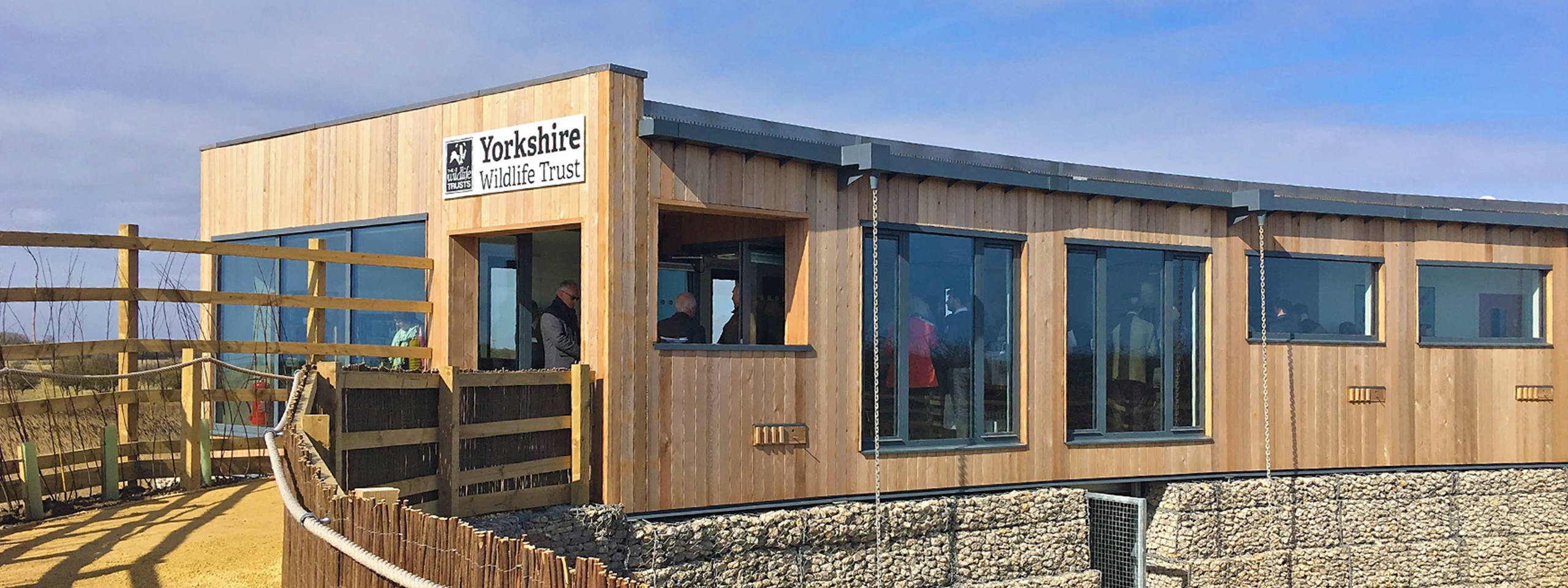 Exterior view of the Yorkshire Wildlife Trust building. The structure features wooden cladding and large windows under a blue sky.