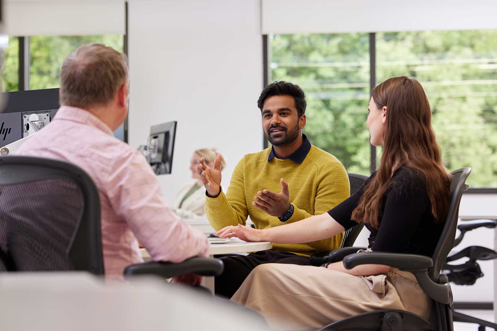 Three individuals engaged in a discussion at an office setting, with natural light illuminating the workspace.