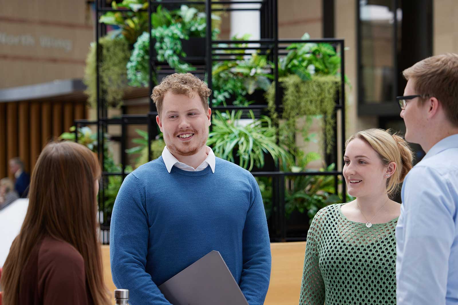 A group of four people engaged in a discussion in a modern interior space adorned with greenery.