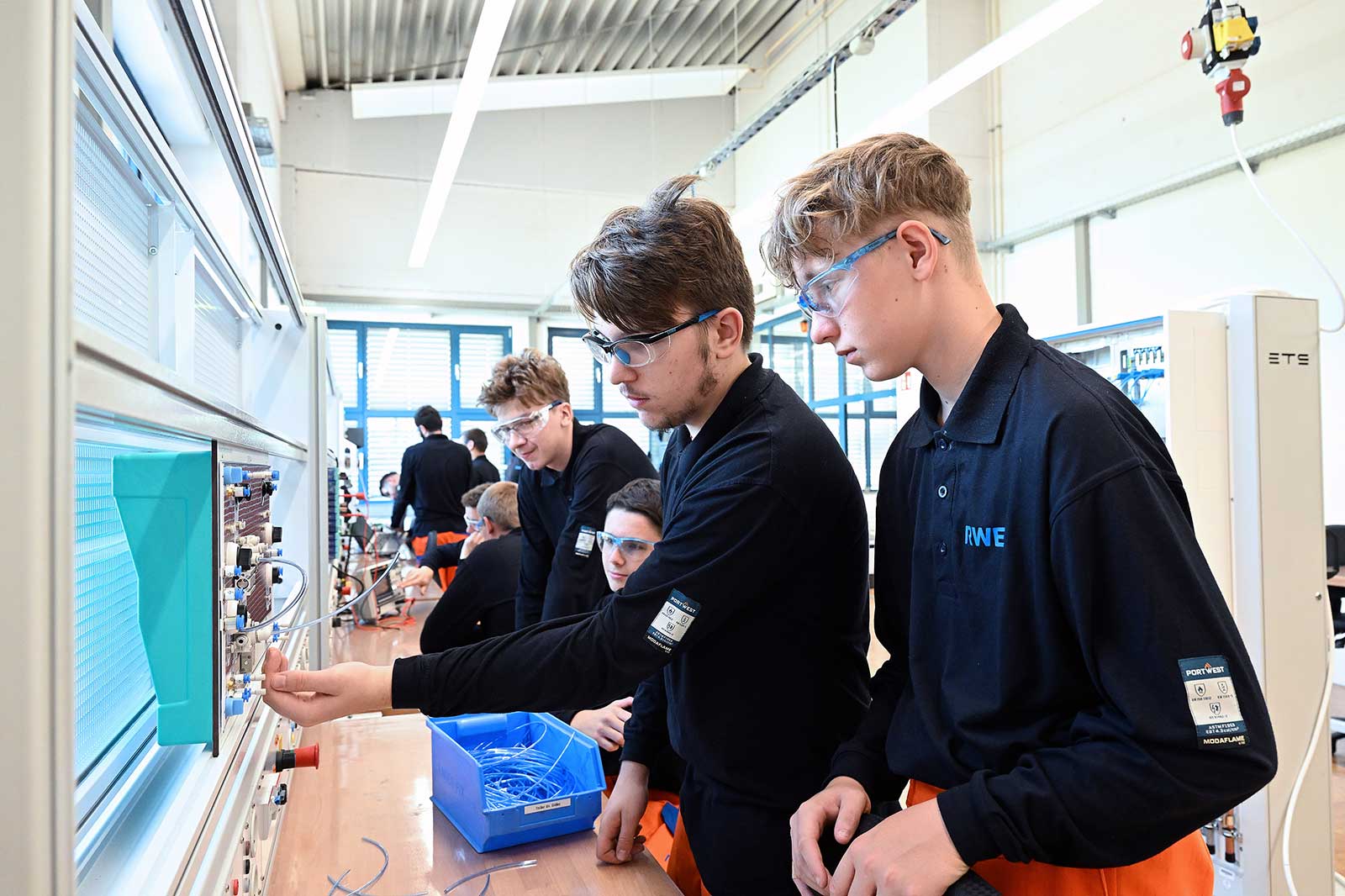 Students working on equipment in a classroom, focusing on practical tasks with tools and materials laid out on tables.