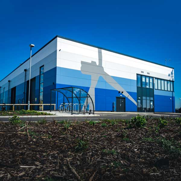 A modern blue and white building with a bicycle shelter, featuring a mural of a wind turbine against a clear blue sky.