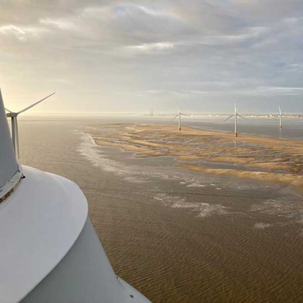 A view from a turbine's perspective, showcasing wind turbines in the distance, at an estuary with sandy shores.