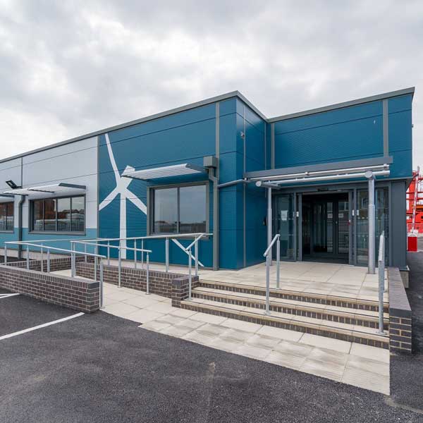 A modern blue building with a wind turbine design, featuring accessible ramps and glass doors under a cloudy sky.